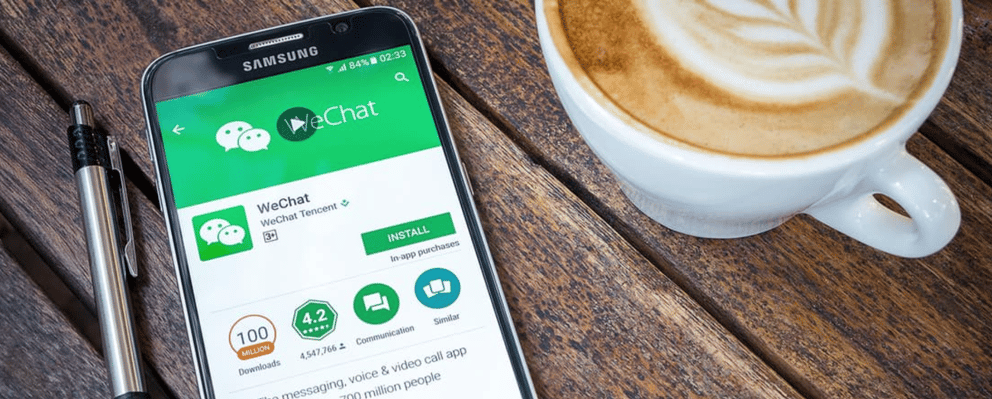 A phone with WeChat displayed on the screen next to a cup of coffee.