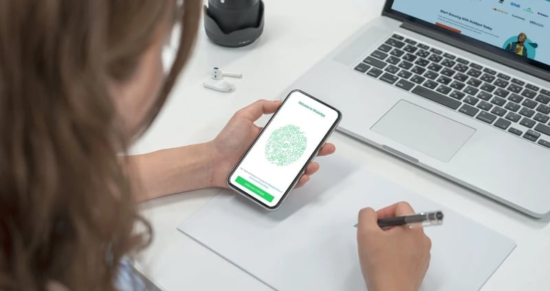 Woman working on laptop with WhatsApp Business open on her phone 